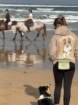 Person with a dog on a beach, with horseback riders in the background.