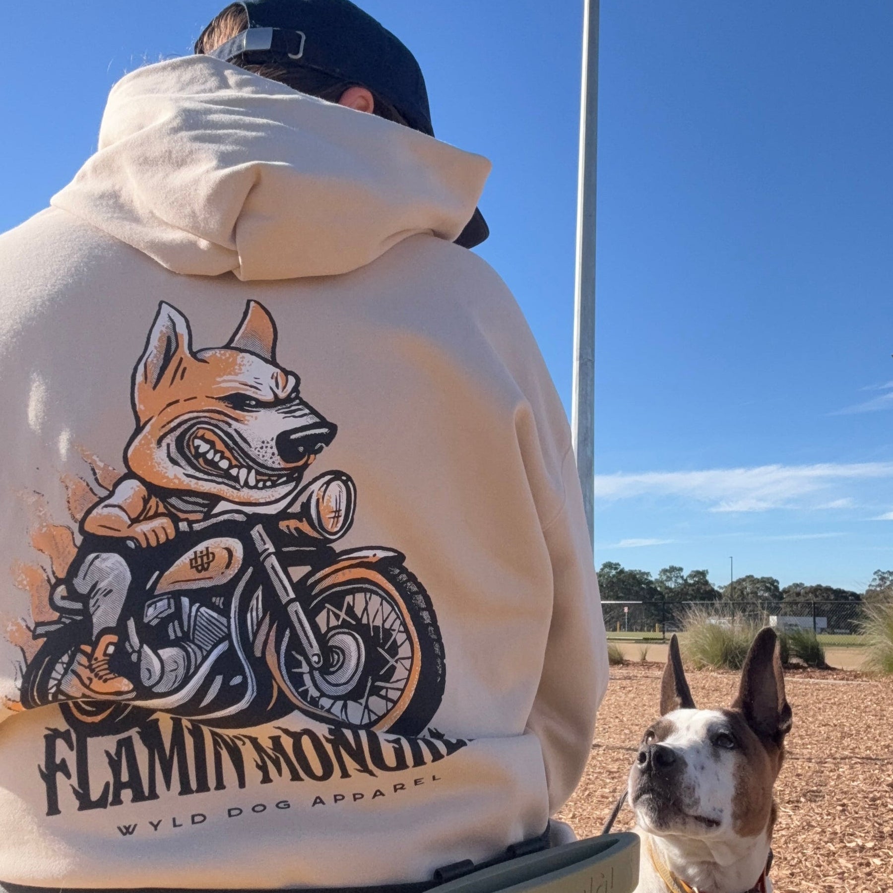 Person wearing a hoodie with a dog graphic and text, standing outdoors with a dog.