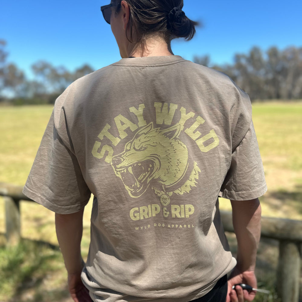 A person wearing a beige t-shirt with the text 'STAY WYLD' and a stylized dog head graphic on the back, standing outdoors.