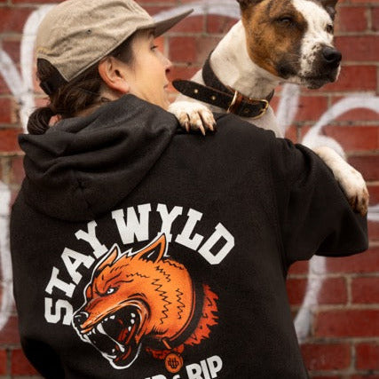 A person wearing a black hoodie with the 'STAY WYLD' logo and a stylized dog design in orange and yellow.