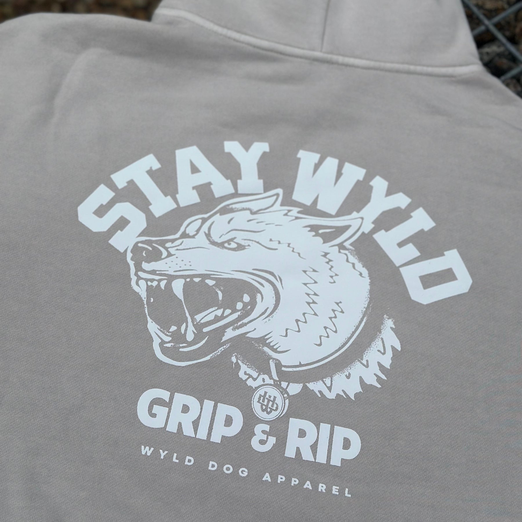 A gray hoodie with the 'STAY WYLD' logo and text 'GRIP & RIP' on the back, featuring a stylized dog head.